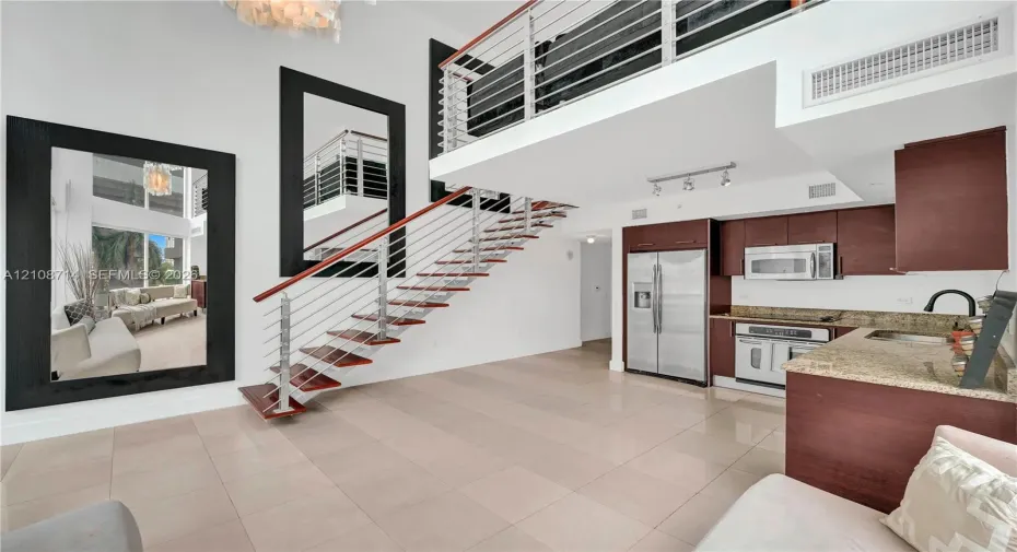 Double-height living area featuring an open staircase with wood treads and horizontal metal railings, tile flooring, built-in cabinetry, and integrated stainless steel appliances