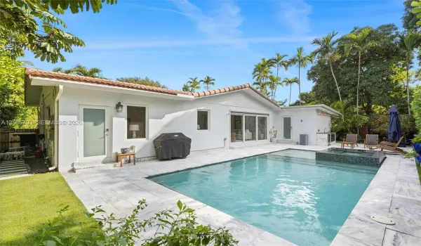 Backyard area featuring an in-ground swimming pool, attached tiled spa, stone paver decking, and exterior wall-mounted lighting