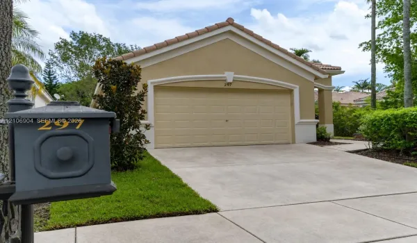 Exterior featuring a neutral-toned stucco facade, a tile roof, an arched garage door, a paved driveway, and a custom metal mailbox