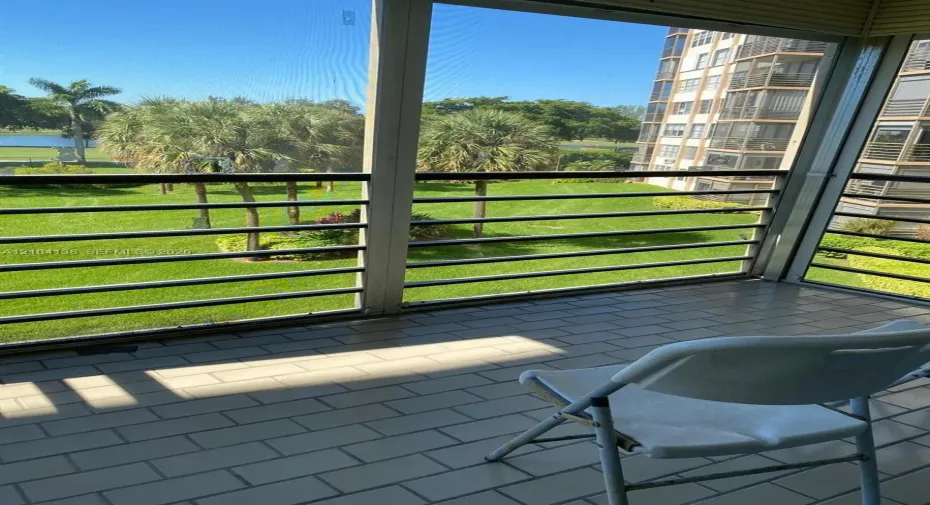 Screened-in balcony featuring tile flooring and metal railings, overlooking a manicured lawn with mature palm trees