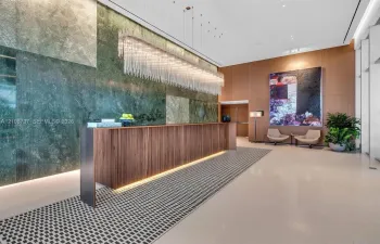 Grand lobby featuring a floor-to-ceiling polished stone accent wall, custom wood-finish reception desk with integrated lighting, elongated linear crystal chandelier, and large-format tile flooring