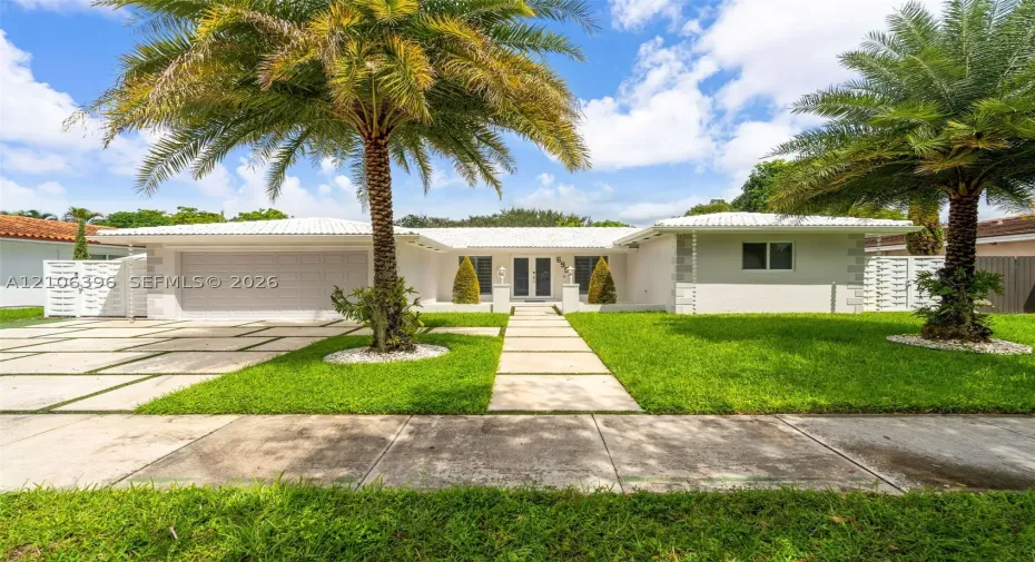 Single-story exterior featuring a light-toned facade, decorative corner quoins, a crisp white tile roof, an integrated garage, and a geometric paver driveway