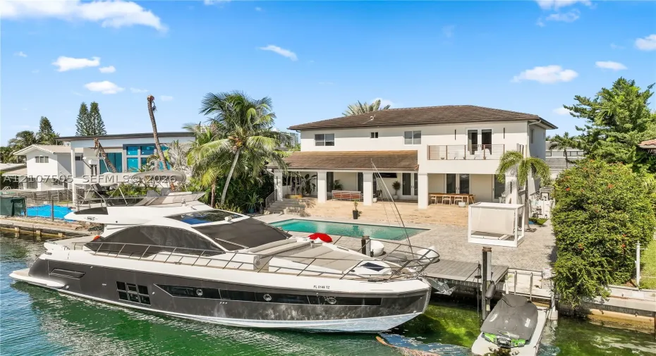 Waterfront property featuring a private boat dock, in-ground swimming pool, stone-paved patio, and two-story exterior with a second-level balcony