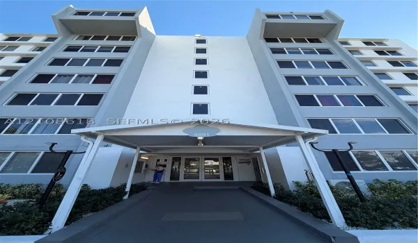 Multi-story concrete exterior featuring a covered entryway with a central pedestrian path, dual-wing facade architecture, and uniform window placement
