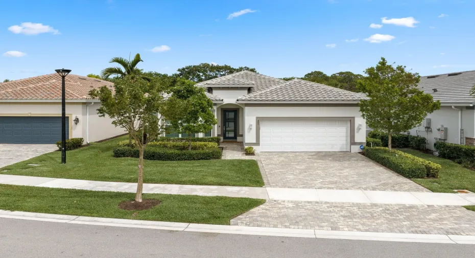 Stucco exterior featuring a tiled roof, paver driveway, two-car garage, and manicured landscaping