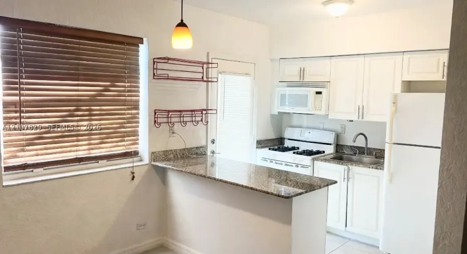 Kitchen featuring a stone-surface breakfast bar, white cabinetry, integrated microwave, and pendant lighting