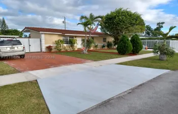 Single-story exterior featuring a clay tile roof, concrete driveway, and white vinyl privacy fencing