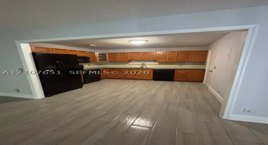 Kitchen featuring wood-finish cabinetry, black appliances, solid-surface countertops, and wood-finish tile flooring