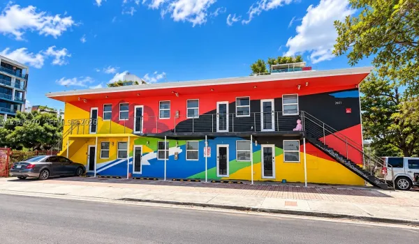 Two-story exterior featuring vibrant multi-colored mural facade, metal staircase with railing, paved parking area, and uniform rectangular window placement