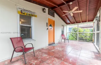 Screened-in porch featuring a terracotta tile floor, exposed wood-beam ceiling, ceiling fan, and built-in wall-mounted light fixtures