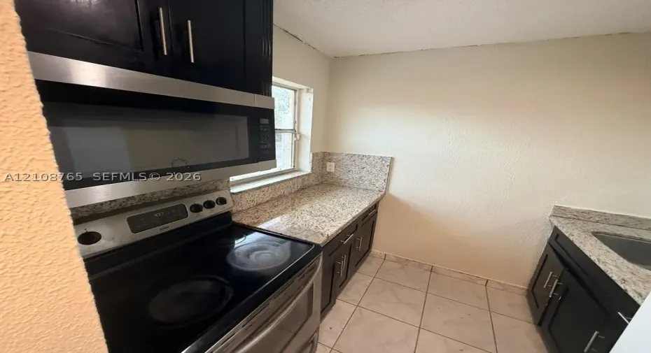 Kitchen featuring dark cabinetry, stone countertops, stainless steel appliances including a built-in microwave and range, and tiled flooring