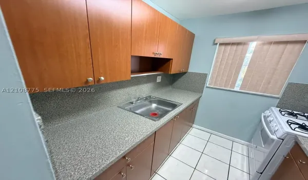 Kitchen featuring wood-finish cabinetry, solid-surface countertops, integrated backsplash, stainless steel drop-in sink, and ceramic tile flooring