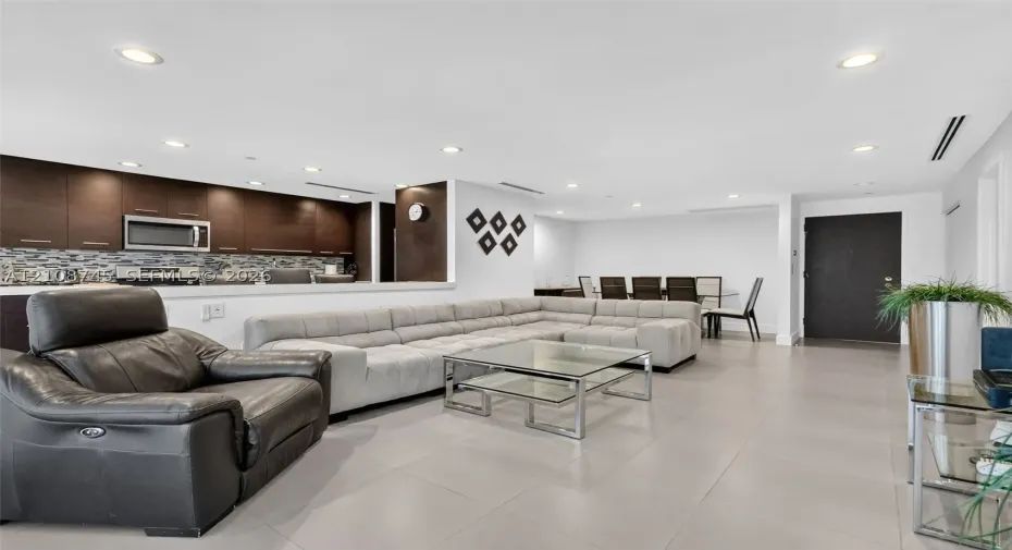 Open-concept space featuring large-format tile flooring, recessed ceiling lighting, dark cabinetry, and a decorative tile backsplash