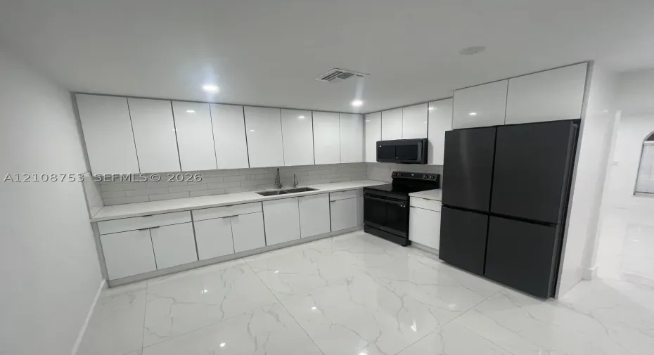 Kitchen featuring gloss-finish white cabinetry, stone-surface countertops, subway tile backsplash, oversized light-colored floor tiles with vein detailing, and integrated black appliances