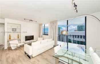 Open-concept living space featuring wood-finish flooring, floor-to-ceiling windows, a private balcony with metal railing, and built-in shelving with integrated counter space