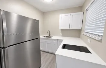 Kitchen featuring white cabinetry, solid surface countertops, a stainless steel refrigerator, a built-in cooktop, and a stainless steel undermount sink with a gooseneck faucet