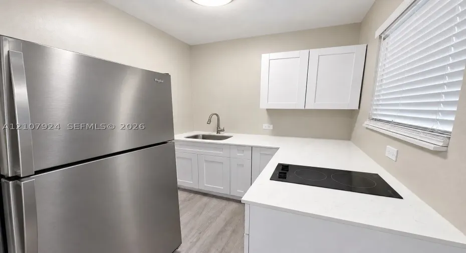 Kitchen featuring white cabinetry, solid surface countertops, a stainless steel refrigerator, a built-in cooktop, and a stainless steel undermount sink with a gooseneck faucet