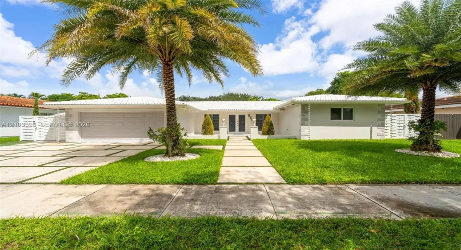 Single-story exterior featuring a light-toned facade, decorative corner quoins, a crisp white tile roof, an integrated garage, and a geometric paver driveway