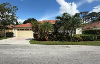 Stucco exterior featuring a terracotta tile roof, attached two-car garage, and manicured landscaping with mature palms