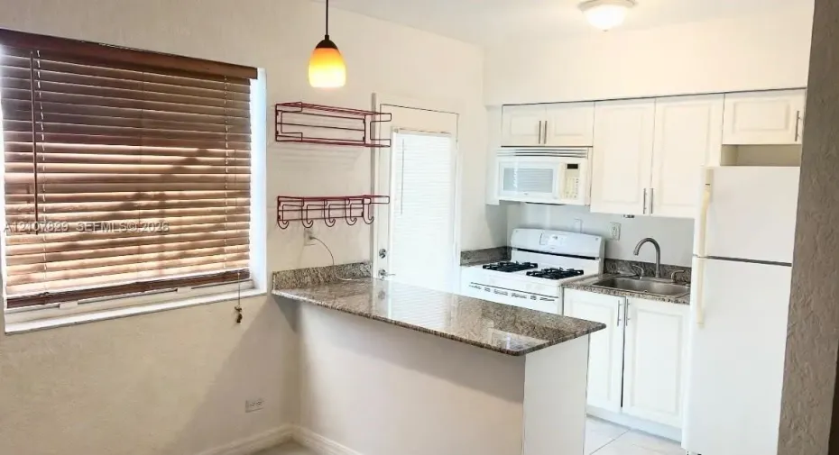 Kitchen featuring a stone-surface breakfast bar, white cabinetry, integrated microwave, and pendant lighting