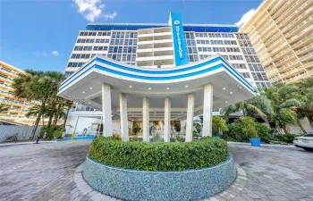 Multi-story exterior featuring a prominent porte-cochère, paved motor court, central circular landscaping, and mosaic tile exterior accents
