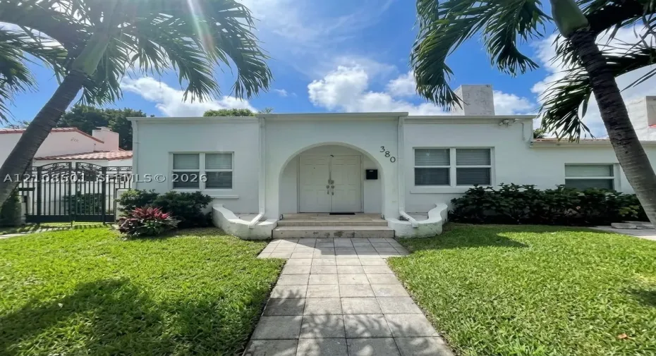 Stucco exterior featuring an arched entryway, double-door entrance, stone-paved walkway, and manicured landscaping