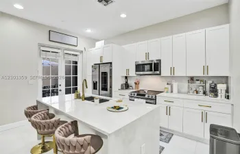 Kitchen featuring white shaker-style cabinetry, quartz countertops with a waterfall-edge island, stainless steel appliances, and gold-finish hardware