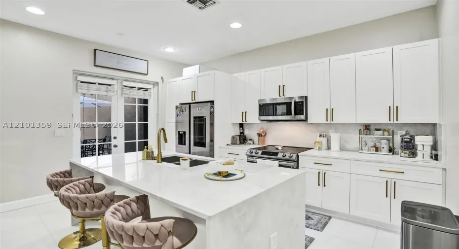 Kitchen featuring white shaker-style cabinetry, quartz countertops with a waterfall-edge island, stainless steel appliances, and gold-finish hardware