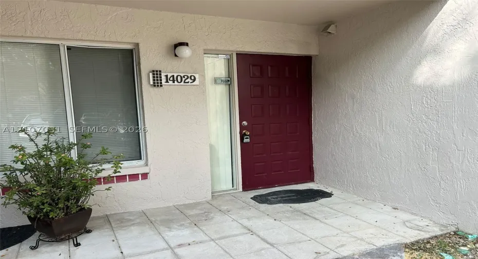 Entryway featuring a solid panel front door, textured exterior stucco, square ceramic tile flooring, and a glass-paneled sidelight