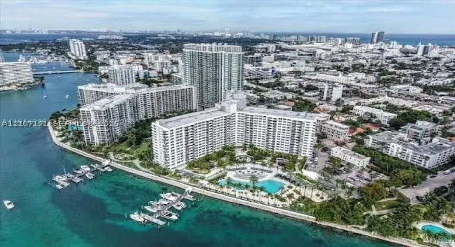 Aerial perspective of a waterfront residential complex featuring a swimming pool, boat slips, and coastal landscaping