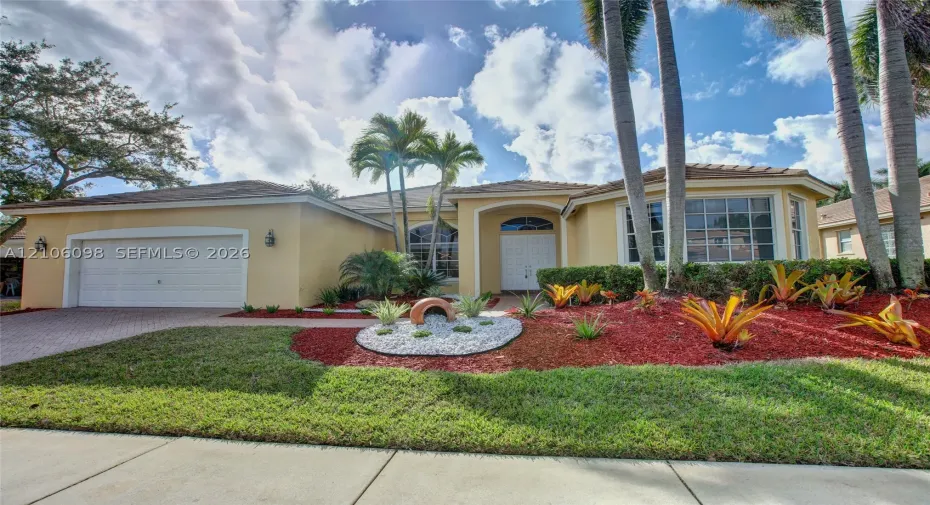 Single-story residence featuring a stucco exterior, multi-pane windows, a paver driveway, an attached two-car garage, and established tropical landscaping