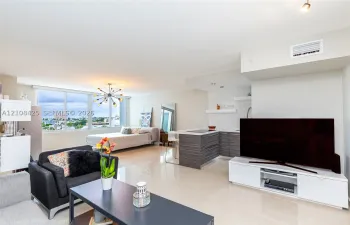 Open-concept interior featuring large-format polished tile flooring, floor-to-ceiling windows, and a kitchen with horizontal-grain cabinetry and a breakfast bar