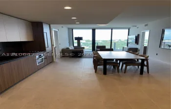 Modern kitchen featuring wood-finish cabinetry, built-in stainless steel oven, stone-surface countertops, recessed ceiling lighting, and floor-to-ceiling glass doors opening to a private balcony