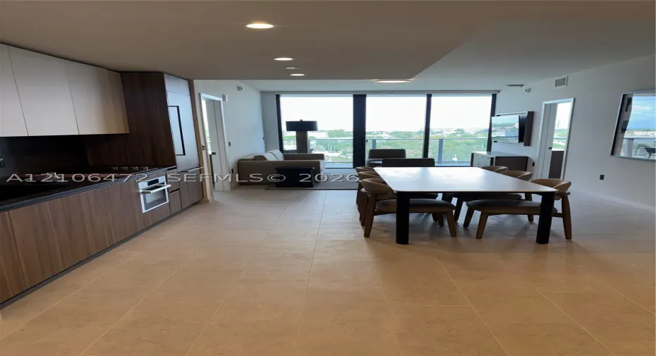 Modern kitchen featuring wood-finish cabinetry, built-in stainless steel oven, stone-surface countertops, recessed ceiling lighting, and floor-to-ceiling glass doors opening to a private balcony