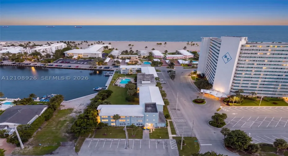 Aerial perspective of property featuring an outdoor swimming pool, direct water frontage, multi-level parking lot, and proximity to the coastline