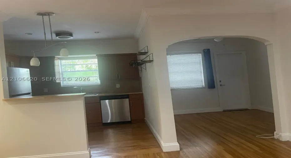 Kitchen featuring wood cabinetry, stainless steel appliances, a peninsula counter, and pendant lighting, opening through an arched entryway to hardwood flooring