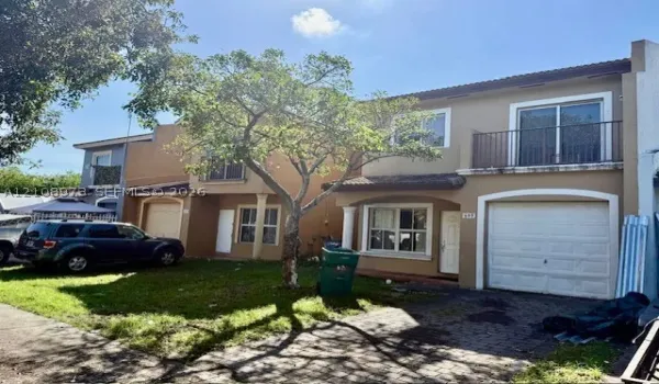 Two-story exterior featuring a stucco facade, single-car garage, second-story balcony with metal railings, and a paved driveway