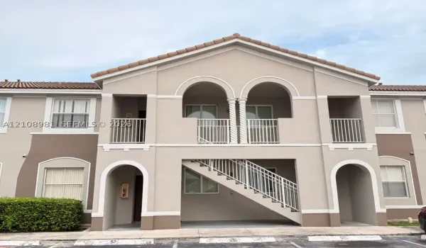 Exterior building facade featuring arched architectural details, twin columns on the upper balcony, clay-tile roofing, and metal stair railings