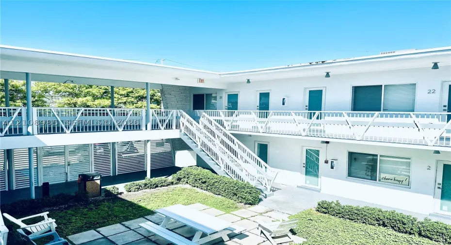 Two-story exterior with white facade, metal staircase, expansive central courtyard, stone-texture siding accents, and paver-stone ground surfacing