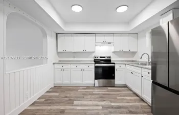 Kitchen featuring white cabinetry, wood-finish flooring, stone-patterned countertops, stainless steel appliances, and a recessed archway with wainscoting