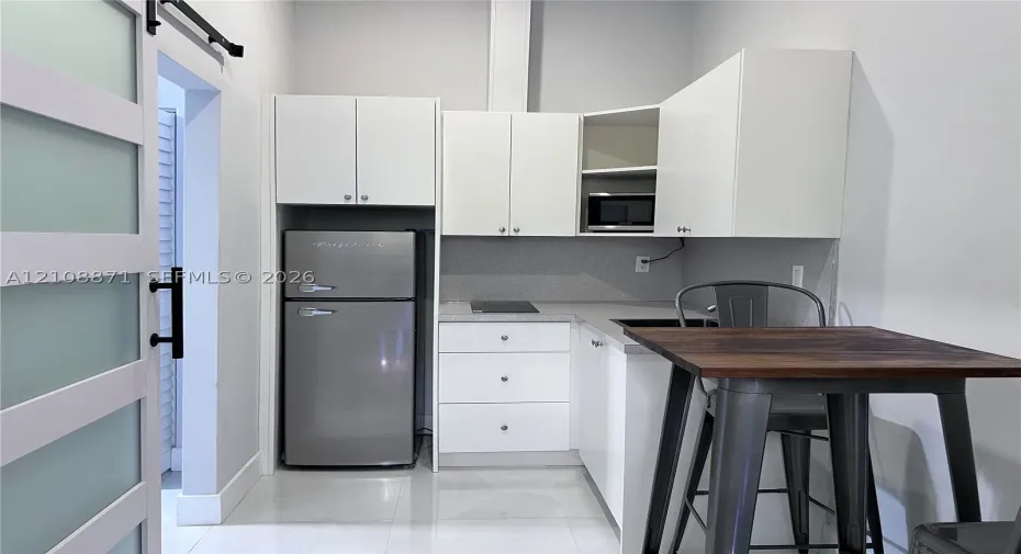 Kitchenette featuring white cabinetry, solid-surface countertops, a stainless-steel refrigerator, a built-in microwave, and a frosted glass sliding barn door