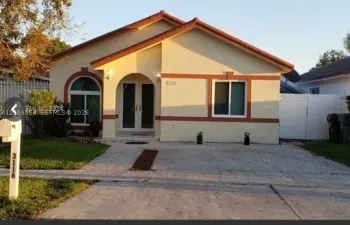 Single-story exterior featuring a stucco facade, arched entryway, double-door entrance, concrete driveway, and clay tile roof