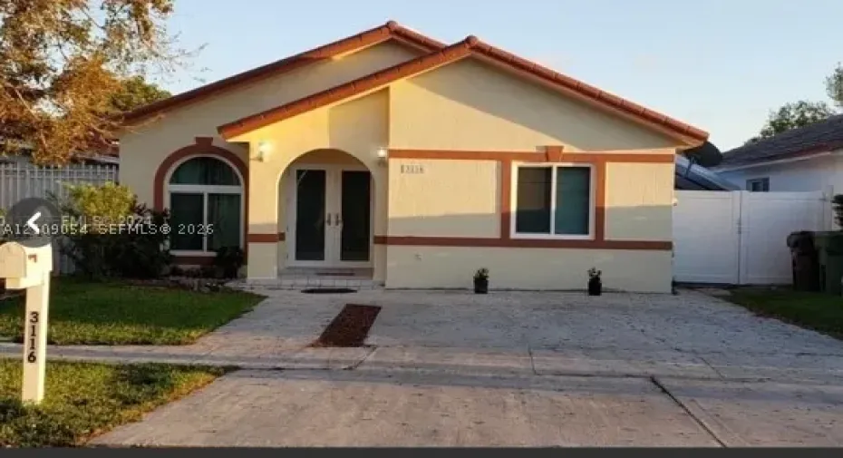 Single-story exterior featuring a stucco facade, arched entryway, double-door entrance, concrete driveway, and clay tile roof