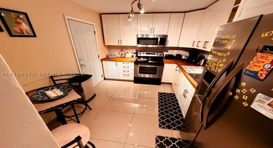 Kitchen featuring white shaker-style cabinetry, wood-finish countertops, stainless steel appliances, and large-format tile flooring