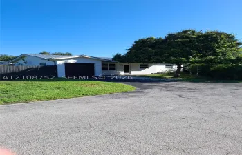 Single-story residence featuring a metal roof, attached garage, paved driveway, and mature landscaping