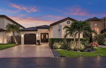 Single-story exterior featuring a tile roof, decorative double entry doors with glass inserts, brick-paver driveway, and professional landscape design