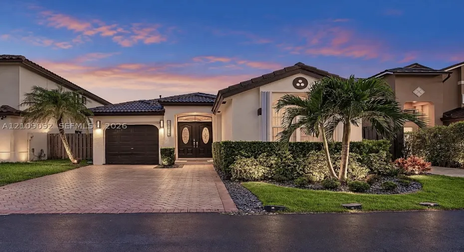 Single-story exterior featuring a tile roof, decorative double entry doors with glass inserts, brick-paver driveway, and professional landscape design