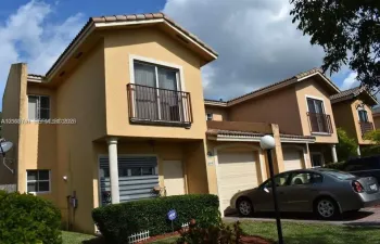 Two-story residence featuring a stucco exterior, integrated garage, upper-level balconies with metal railings, and decorative columns