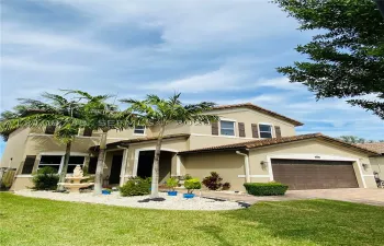 Two-story residence featuring a tile roof, stucco exterior, attached two-car garage, paver driveway, and landscaped front yard with palm trees
