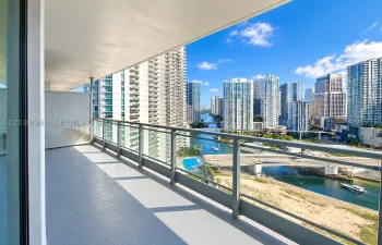 Covered balcony with smooth-finish concrete flooring and metal railings, featuring an urban skyline and waterway backdrop